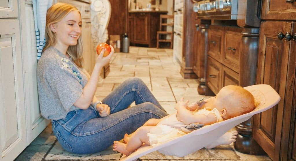 Hannah Uhl assise sur le sol de la cuisine avec bébé sur le point de manger de la pomme